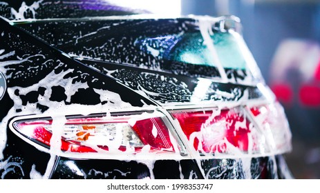 Car wash concept. Front view of white sports car covered with water, washing foam, and soap on hood and bumper. Professional car detailing and commercial cleaning service concept. Wet car background - Shutterstock ID 1998353747