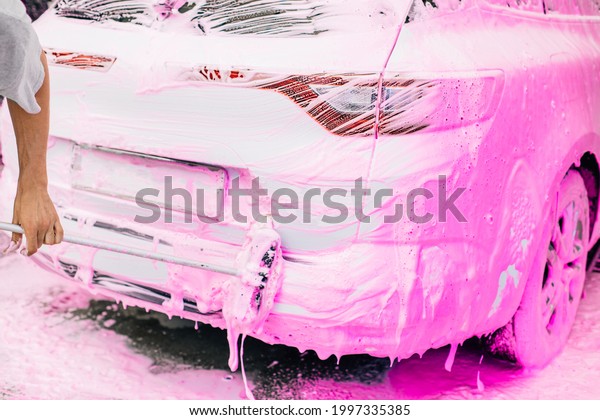 Car wash concept, Front view of white\
sports car covered with pink foam, Professional cleaning and car\
wash, Man washing car with high pressure\
water