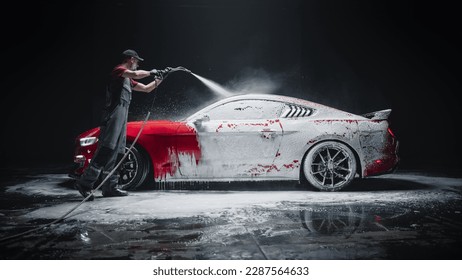 Car Wash Expert Using Water Pressure Washer to Clean a Red Modern Sportscar. Adult Man Washing Away Dirt, Preparing an American Muscle Car for Detailing. Creative Cinematic Photo with Luxury Vehicle
