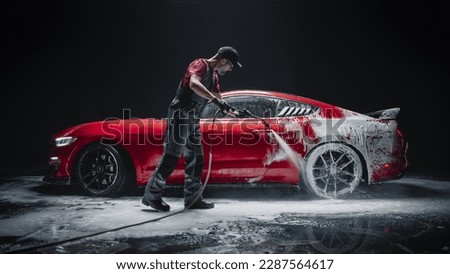 Car Wash Expert Using Water Pressure Washer to Clean a Red Modern Sportscar. Adult Man Washing Away Shampoo, Preparing a Muscle Car for Detailing. Creative Low Key Photo with Sport Vehicle
