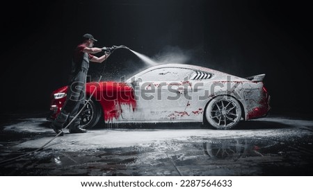Car Wash Expert Using Water Pressure Washer to Clean a Red Modern Sportscar. Adult Man Washing Away Dirt, Preparing an American Muscle Car for Detailing. Creative Cinematic Photo with Luxury Vehicle