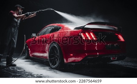 Car Wash Expert Using Water Pressure Washer to Clean a Red Modern Sportscar. Adult Man Washing Away Dirt, Preparing an American Muscle Car for Detailing. Creative Cinematic Footage with Luxury Vehicle