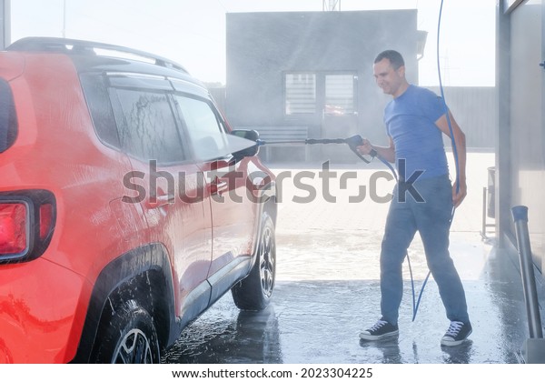 Car wash with high pressure water. Man washes the\
car outdoors, car wash