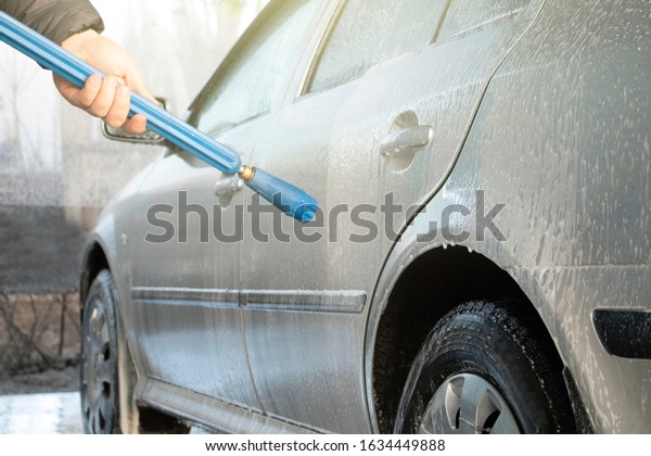 Car wash. A man washes a car\
under the pressure of water and rubs the glass. Car care\
concept