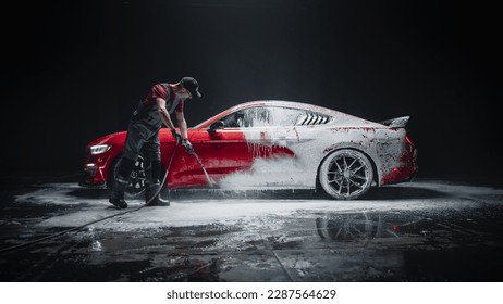 Car Wash Specialist Using Pressure Washer to Rinse a Red Modern Sportscar. Adult Man Washing Away Dirt, Preparing a Tuned Car for Detailing. Creative Cinematic Photo in Studio