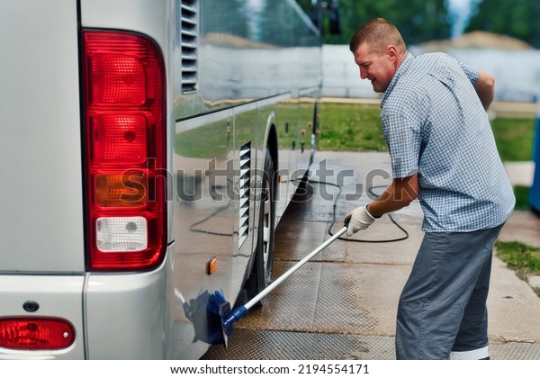 Car wash worker manually\
washes large bus with brush in open parking lot on summer day.\
Preparation of transport for transportation of passengers. Real\
workflow.