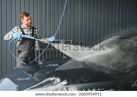 A car wash worker is using high pressure water gun for car washing.
