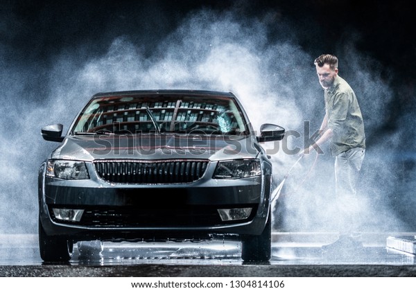 A car\
washer washes a gray car with a high-pressure washer at night on\
the street. Expensive advertising\
photography