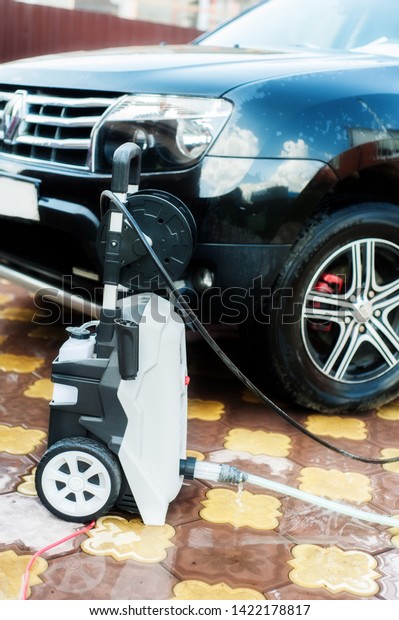 Car washing. Cleaning car\
using high pressure water. Portable car wash machine next to black\
machine