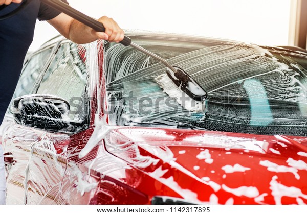 Car washing concept. Man
cleaning vehicle Using brush and foam, front window. Selective
detail focus.