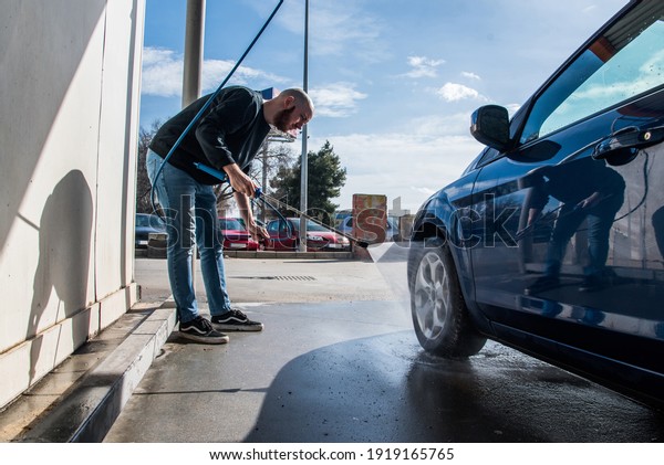 Car washing concept. Man using high pressure\
water to clean a tire of his\
car