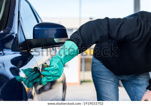 Car washing. Detail of a man\'s hand\
wearing a green glove cleaning his car using a\
sponge.