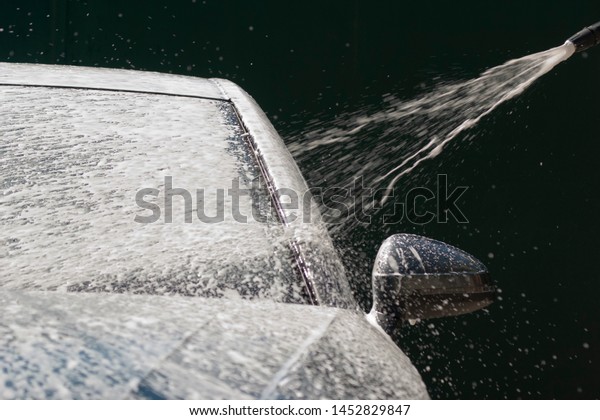 Car washing with\
high pressure water jet. Water and foam under pressure flies toward\
the car body. Close-up view
