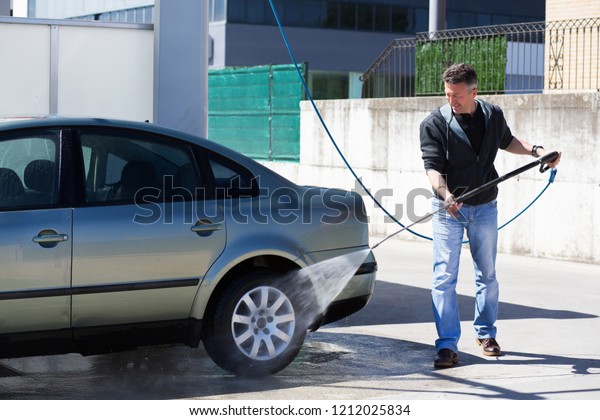 Car washing. Man cleaning car using high pressure\
water and brush outdoor