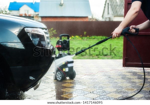 Car washing. A man washes a car with a\
portable washer with a high-pressure\
hose
