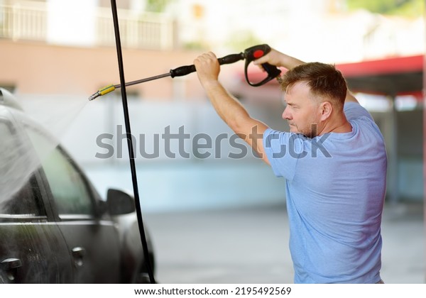 Car washing. Mature caucasian man\
cleaning automobile using high pressure jet\
water.