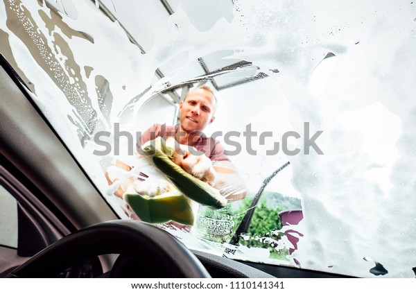 Car washing process: man washes front car window with\
soap 