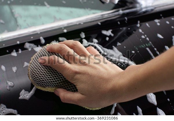 Car washing process when the human hand holding
wiper and washing  luxury car full covered with  white foam with
bubbles or car wash close
up.