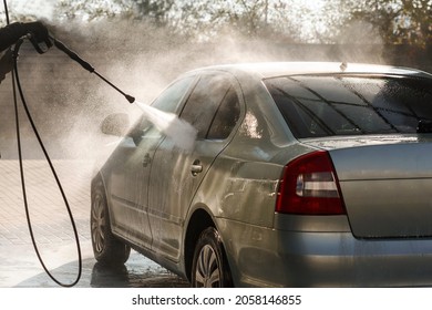 Car Is Washing Under Strong Water Pressure From A Hose On The Automatic Sink, Backlight, Outside. Cleaning Car Concept.