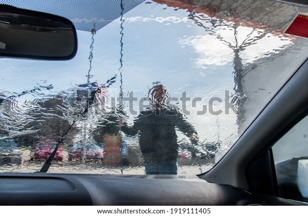 Car washing. View\
from inside the car of a man cleaning his car using high pressure\
water on a sunny day.