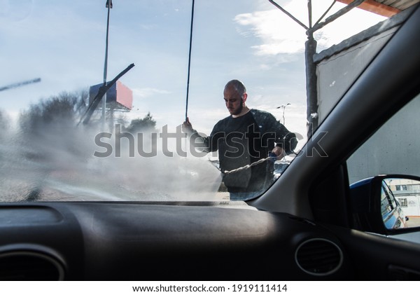 Car washing. View
from inside the car of a man cleaning his car using high pressure
water on a sunny day.