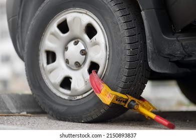 Car wheel blocked by wheel lock. Illegal parking of automobile. Wheel of automobile was locked with clamped tire boot. Parking violations. Illegally parked car.