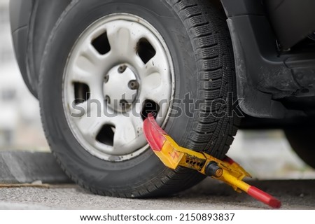 Car wheel blocked by wheel lock. Illegal parking of automobile. Wheel of automobile was locked with clamped tire boot. Parking violations. Illegally parked car.