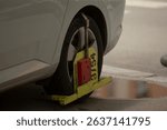 A car wheel has been immobilized by a large boot in a busy urban area, emphasizing the importance of vehicle enforcement measures and the necessity of following parking regulations