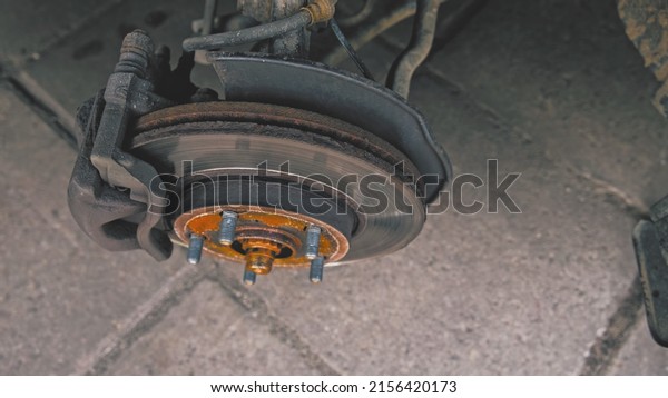 Car\
Wheel Hub with Brake Disc and Brake Pad Exposed during Tyre Change\
at Garage Workshop with Lug Nuts Laying on\
Ground
