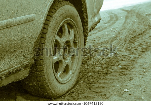 Car wheel on a dirt road.\
Off-road tire covered with mud, dirt terrain. Outdoor, adventures\
and travel. Car tire close-up in a countryside landscape with a\
muddy road