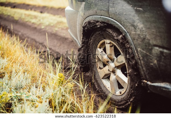 Car wheel on a dirt road. Off-road tire covered with\
mud, dirt terrain. Outdoor, adventures and travel suv. Car tire\
close-up in a countryside landscape with a muddy road. Four wheel\
truck in mud.