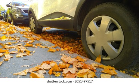 Car wheel on road. Yellow fallen maple leaves on asphalt road. Golden autumn street. Travelling. Driving. Automobile hubcap. Protection auto. Fall season. Vehicle tire. Free parking. Autumnal day.