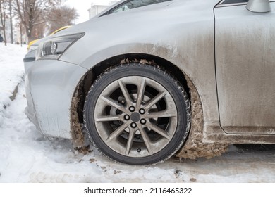 Car Wheel On The Snow In Winter After Driving On Dirty Chemicals, Close-up, Side View. Wet Dirty Snow Sticking To The Front Fender Of The Car. 