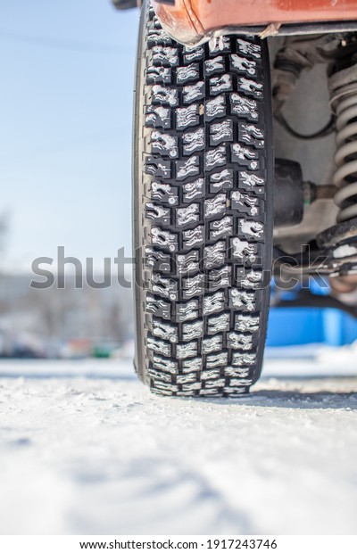 Car wheel on snow in winter close-up. The suspension\
and chassis of the car are visible. The car is parked in a snowy\
parking lot.