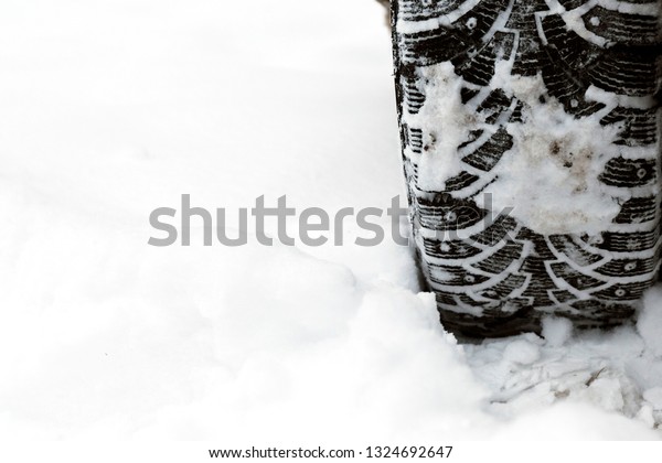 Car wheel with winter studded tires on  background\
of snow.