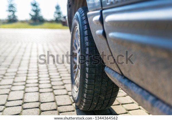 Car wheel with a\
winter tire in an off-road car, standing on a paving stone. Home\
garden in the background.\
