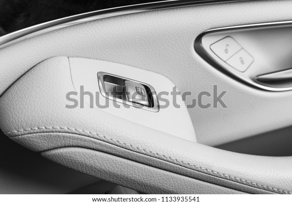 Car white leather interior details of\
door handle with windows controls and adjustments. Car window\
controls of modern car. Car detailing. Black and\
white