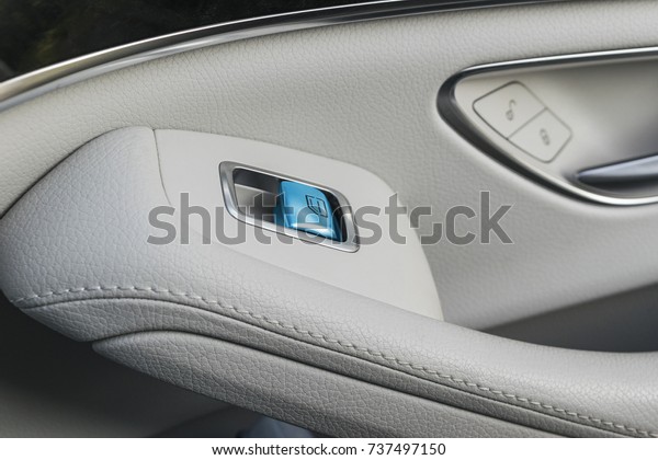 Car white leather interior details of door handle\
with windows controls and adjustments. Car window controls blue\
button of modern car.