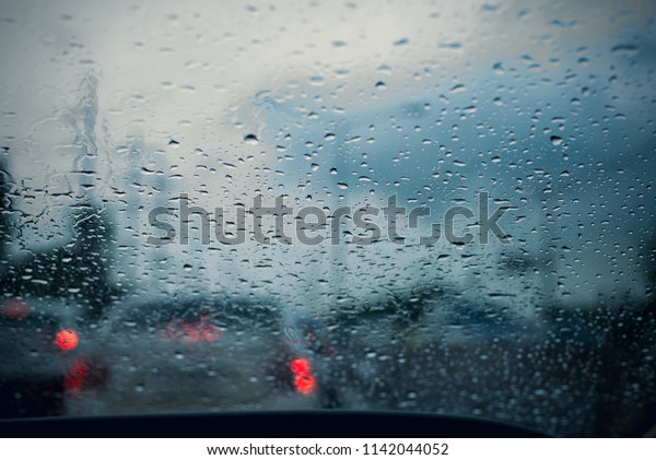 Car window with rain drops on\
glass or the windshield,Blurred traffic on rainy day in the\
city