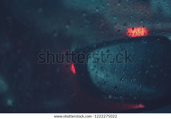 Car window with rain drops window on glass
rearview mirror with road light bokeh glass background blurred.
City life in night in rainy season night storm raining car driving
concept. soft focus.