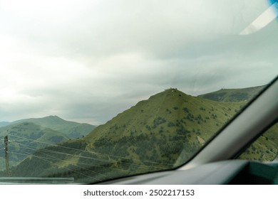 A car window shows a mountain range with a cloudy sky