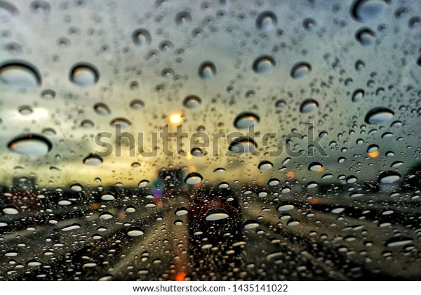 car windshield caught by rain droplet.
car in a traffic jammed highway during storm. close up shoot on
water drop blurred car and dark cloud
background.