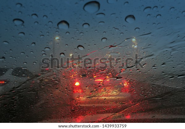 car windshield caught by rain droplet.\
car in a traffic jammed highway during storm. close up shoot on\
water drop blurred car and dark cloud\
background.