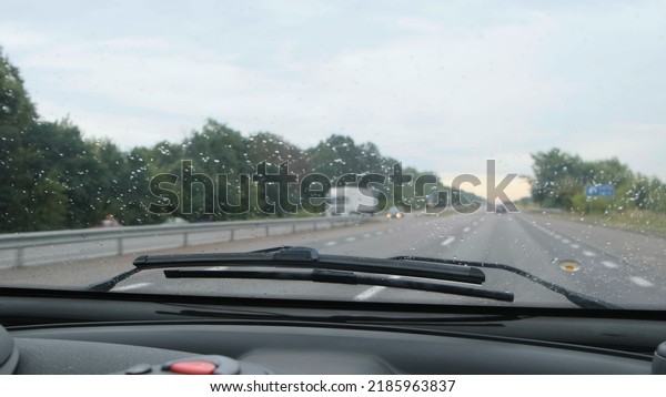 Car windshield during light rain. Car moves by rainy\
day along the highway, the wind blows off raindrops from front\
glass of car