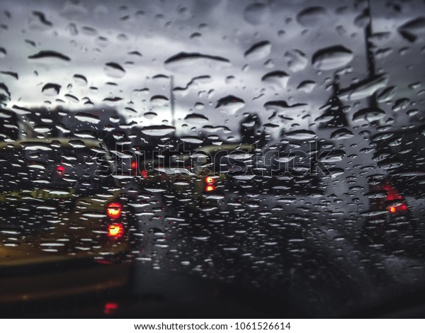 Car windshield full of raindrops and cars in the\
background 