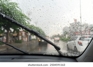 Car windshield with rain drops and frameless wiper blade closeup. Car windshield wiper cleaning water drops from glass while driving