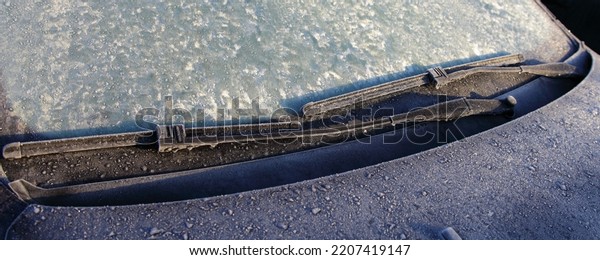 Car windshield wipers blades on frozen glass with\
hoarfrost closeup