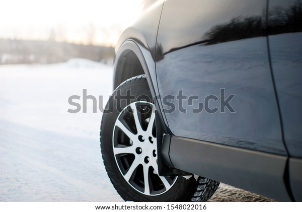 Car winter tires on a\
car standing on a winter den on a background of forest and sunset.\
Selective focus.