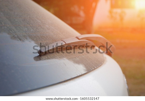 Car wiper blade behind side.Glass Dirty car,Dirty\
back glass of the car with a wiper blade,Rear Car glass covered in\
dust after driving on a dirt road.Car wiper blade for cleaning\
glass.Close up.