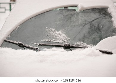Car wiper blades clean snow from car windows. Flakes of snow covered the car with a thick layer. Safe driving with working wipers and clean windshield. Selective focus